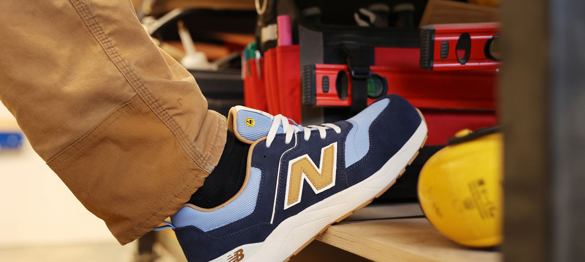 New Balance Elite Lite safety trainer in navy and tan, worn in a joinery workshop